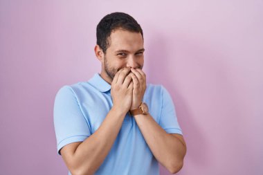 İspanyol adam pembe arka planda gülüyor ve utanıyor kıkır kıkır kıkır gülüyor eller, dedikodular ve skandal konseptiyle ağzını kapatıyor 