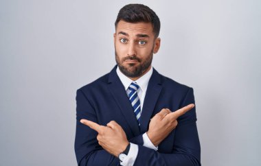 Yakışıklı İspanyol takım elbiseli ve kravatlı adam her iki tarafı da parmaklarıyla işaret ediyor, farklı yönlere bakıyor. 