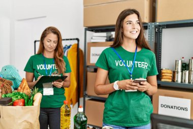 Anne ve kızı gönüllü üniforması giyip listeye yazıyorlar ve yardım merkezinde akıllı telefon kullanıyorlar.