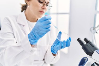 Laboratuvarda pipet kullanan, bilim adamı üniforması giyen İspanyol genç bir kadın.