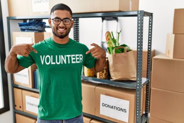 Gönüllü genç Hintli bir adam bağış kutusunu tutuyor. Yüzünde gülümsemeyle kendinden emin görünüyor. Kendini gururlu ve mutlu olarak gösteriyor.. 