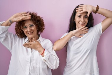 İspanyol anne ve kızı pembe arka plan üzerine gündelik beyaz tişört giyip güler yüzlü bir şekilde ellerini göstererek dikizleme oyunu oynuyorlar. Şaşırdım ve çıktım. 
