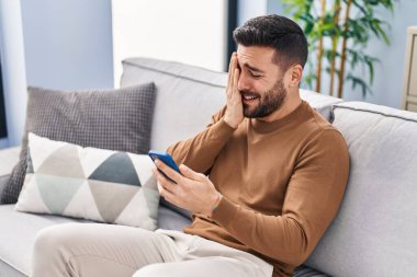 Evdeki kanepede oturan, akıllı telefon kullanan genç bir İspanyol.