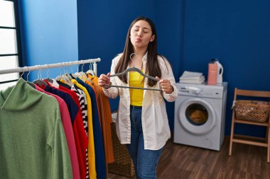 Young latin woman putting clean laundry on hangers looking at the camera blowing a kiss being lovely and sexy. love expression. 