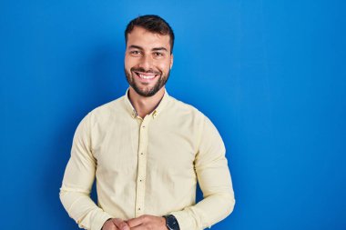 Handsome hispanic man standing over blue background with a happy and cool smile on face. lucky person. 