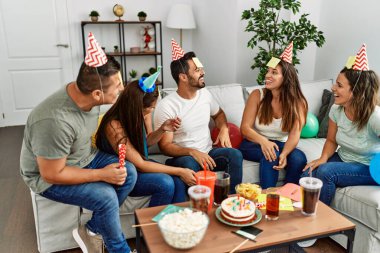 Group of young hispanic friends having birthday party playing funny game at home.