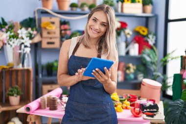 Young caucasian woman florist smiling confident using touchpad at florist