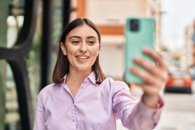 Genç İspanyol kadın gülümsüyor. Kendine güveni tam. Sokakta akıllı telefonun yanında selfie çekiyor.