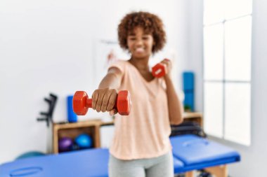 Young african american woman doing rehab using dumbbells at clinic