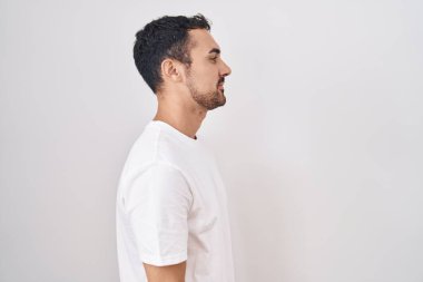 Handsome hispanic man standing over white background looking to side, relax profile pose with natural face and confident smile. 