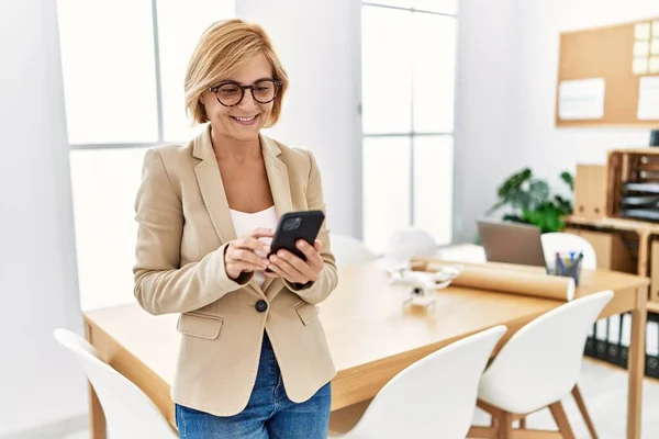 Middle age blonde woman using smartphone working at architecture studio