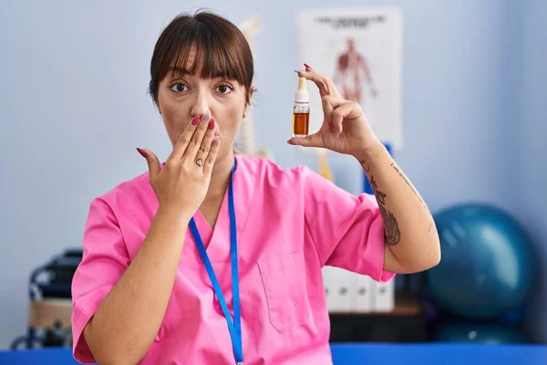 若いブルネットの女性は手で口をカバー理学療法クリニックでCbd油を保持し ショックを受け 間違いを恐れています 驚きの表情 — ストック写真