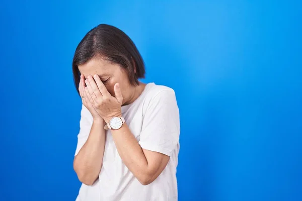 中年惊慌失措的女人站在蓝色的背景上 脸上挂着忧郁的表情 一边哭一边用手捂住脸 抑郁症的概念 — 图库照片