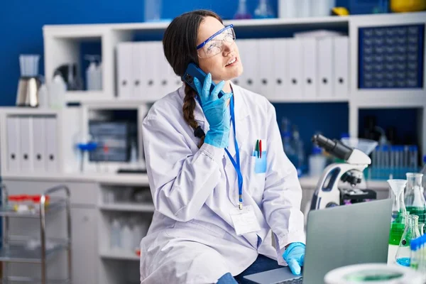 Young woman scientist using laptop talking on the smartphone at laboratory