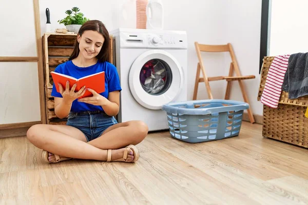 若い白人女性読書本洗濯室で洗濯機を待っています — ストック写真