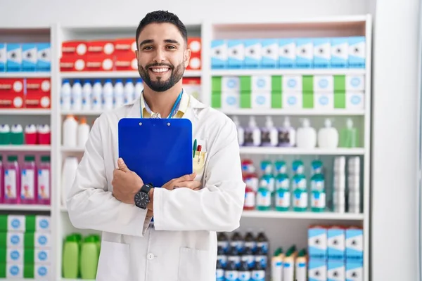年轻的Arab男子药剂师带着自信的笑容在药店拿着剪贴板 — 图库照片