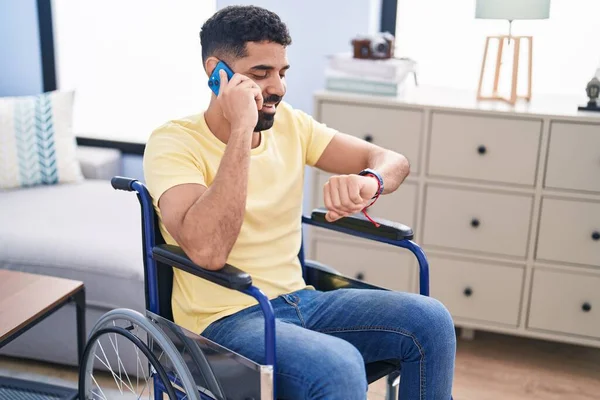 Young Arab Man Talking Smartphone Looking Watch Sitting Wheelchair Home — ストック写真