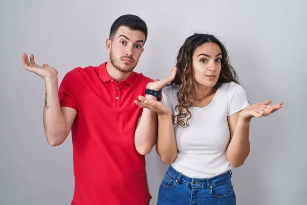 Young Hispanic Couple Standing Isolated Background Clueless Confused Expression Arms — Stock fotografie