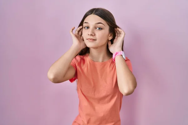 Adolescente Chica Pie Sobre Fondo Rosa Tratando Escuchar Ambas Manos —  Fotos de Stock