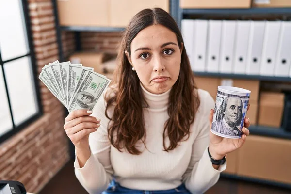 Young hispanic woman working at small business ecommerce holding money and piggy bank depressed and worry for distress, crying angry and afraid. sad expression.