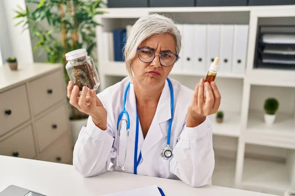 Middle age woman doctor holding cbd oil depressed and worry for distress, crying angry and afraid. sad expression.