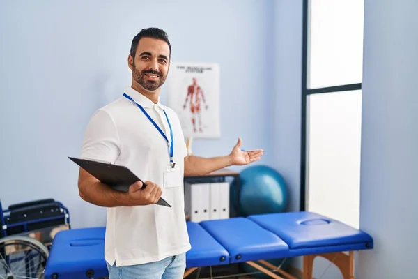 Joven Fisioterapeuta Hispano Sonriendo Confiado Sujetando Portapapeles Clínica Rehabilitación — Foto de Stock