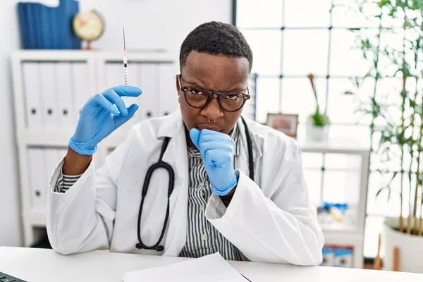 Young african doctor man holding syringe at the hospital feeling unwell and coughing as symptom for cold or bronchitis. health care concept.