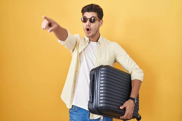 Νεαρός Ισπανόφωνος Κρατώντας Βαλίτσα Πηγαίνοντας Καλοκαιρινές Διακοπές Δείχνοντας Δάχτυλο Έκπληκτο — Φωτογραφία Αρχείου