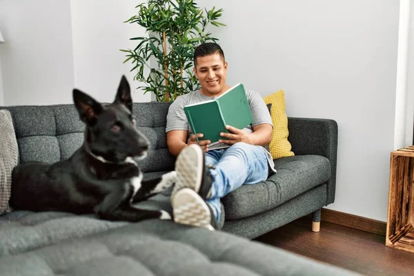 Jovem Hispânico Ler Livro Sentado Sofá Com Cão Casa — Fotografia de Stock