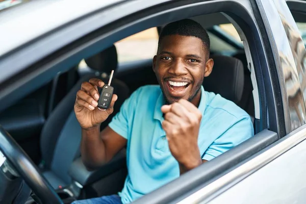 Young african american man holding key of new car with cheerful expression at street