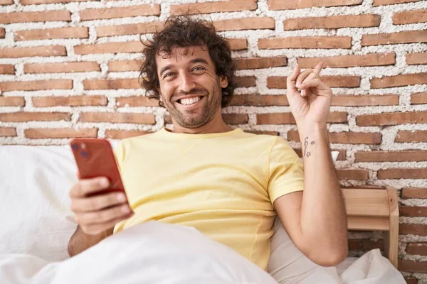 Spanyol Genç Adam Yatağın Üzerinde Akıllı Telefon Kullanıyor Gülümseyerek Mutlu — Stok fotoğraf