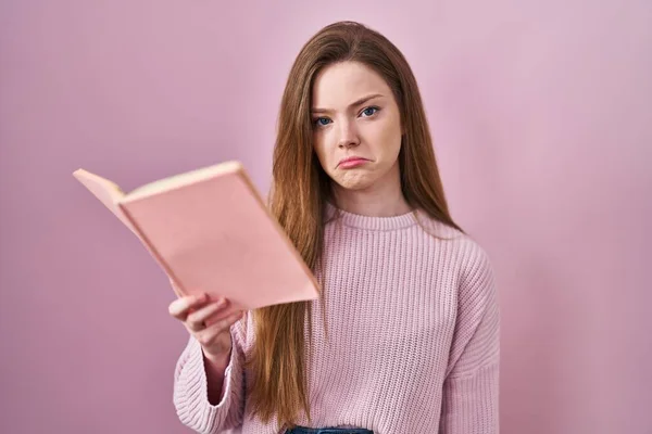 Young caucasian woman reading a book over pink background depressed and worry for distress, crying angry and afraid. sad expression.