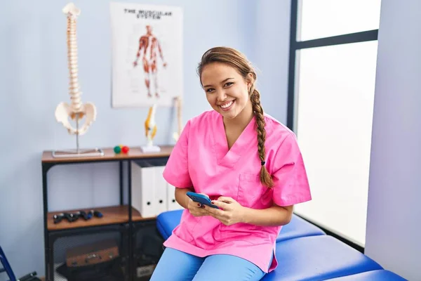 Νεαρή Όμορφη Ισπανίδα Φυσιοθεραπεύτρια Χαμογελά Αυτοπεποίθηση Χρησιμοποιώντας Smartphone Στην Κλινική — Φωτογραφία Αρχείου