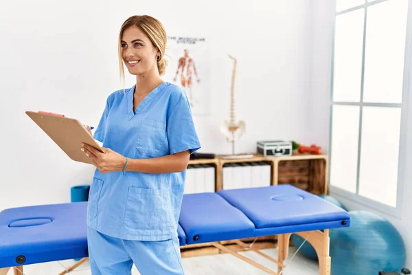 Joven Fisioterapeuta Caucásica Mujer Sonriendo Feliz Escribiendo Lista Verificación Clínica —  Fotos de Stock