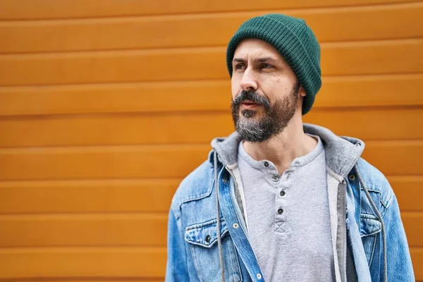 Genç kel adam, izole ahşap arka planda ciddi bir ifadeyle yan tarafa bakıyor.