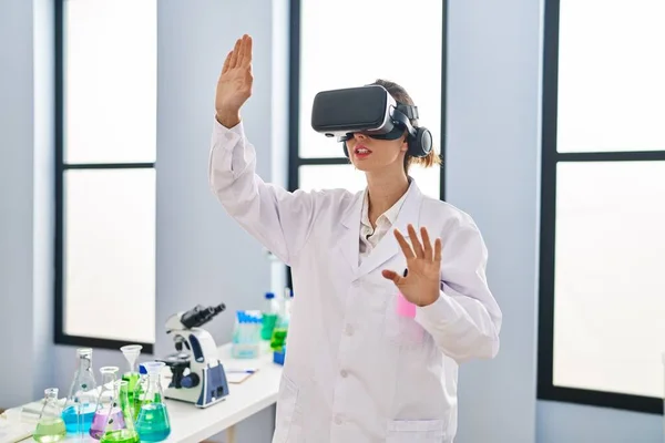 Young woman wearing scientist uniform using virtual reality goggles at laboratory