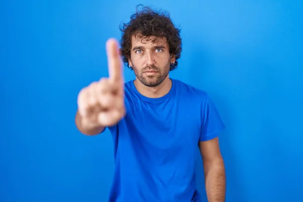 Spaanse Jongeman Staat Blauwe Achtergrond Wijzend Met Vinger Omhoog Boze — Stockfoto