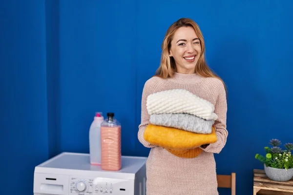 Hispanic woman holding folded laundry after laundry winking looking at the camera with sexy expression, cheerful and happy face.