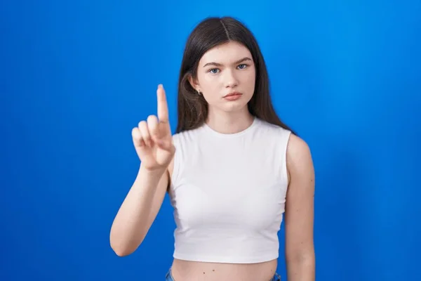 Młoda Biała Kobieta Stojąca Nad Niebieskim Tłem Wskazująca Palcem Górę — Zdjęcie stockowe