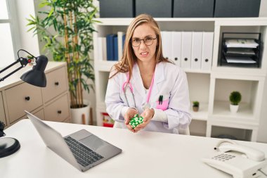 Sarışın kadın elinde haplardan bihaber ve kafası karışık bir ifade tutuyor. şüphe kavramı. 