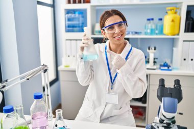 Young brunette woman working at scientist laboratory smiling happy pointing with hand and finger 
