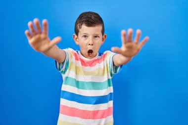 Kafkasyalı genç mavi arka planda duruyor. Avuçlarıyla jesti durduruyor. Öfkeli ve hayal kırıklığı dolu bir ifade. 