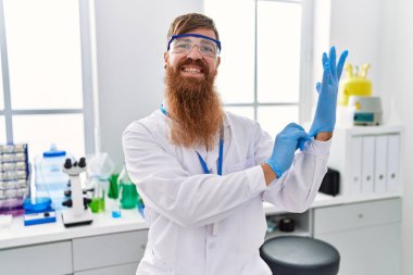 Laboratuvarda eldiven giyen, bilim adamı üniforması giyen genç bir kızıl.