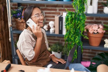 Çiçekçide dizüstü bilgisayar kullanarak konuşan güzel İspanyol çiçekçi kadın.