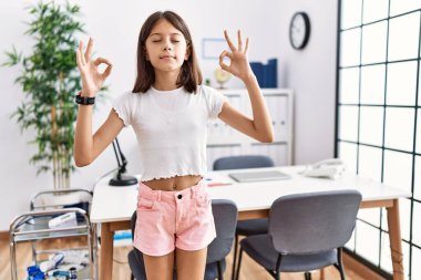 Genç İspanyol kız pediatri kliniğinde rahatlamış ve parmaklarıyla meditasyon hareketi yaparken gözleri kapalı gülümsüyor. yoga konsepti. 