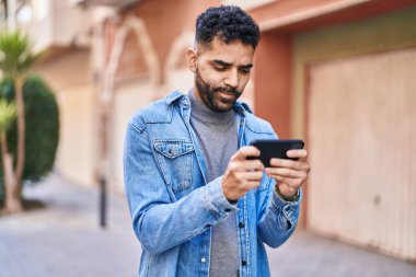 Young hispanic man watching video on smartphone at street