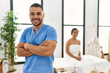 Latin erkek ve kadın fizyoterapi üniforması giyiyorlar. Güzellik merkezinde kollarını kavuşturmuş bekliyorlar.