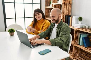 Genç İspanyol çift evde masada dizüstü bilgisayar kullanarak mutlu bir şekilde gülümsüyor..