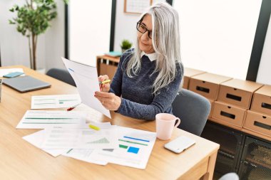 Ofiste çalışırken gülümseyen beyaz saçlı iş kadını.