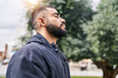 Young hispanic man breathing with closed eyes at park